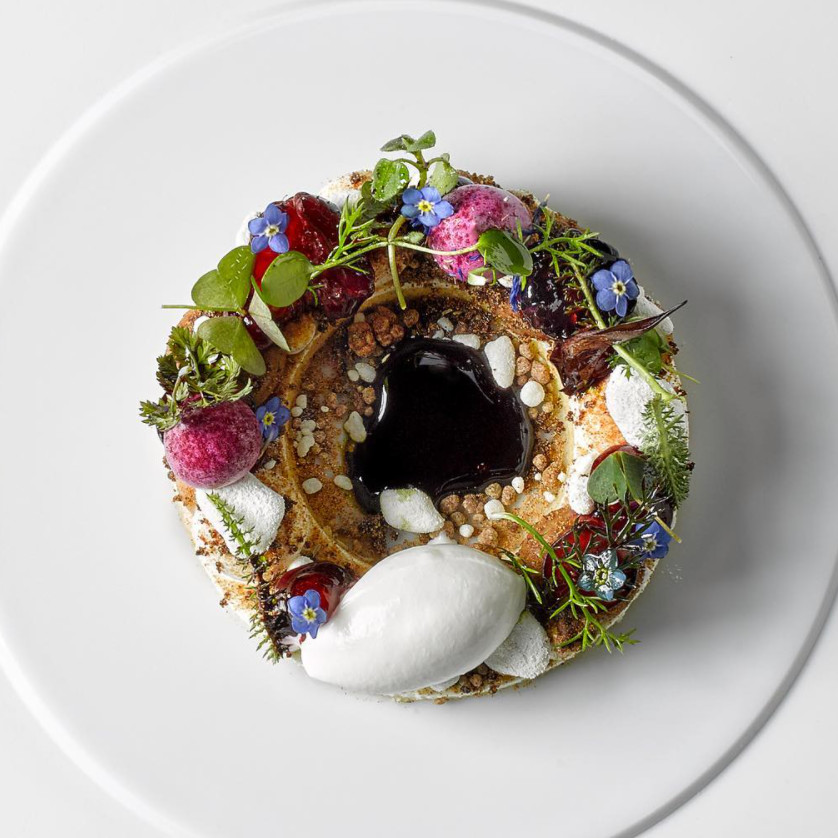 Kunstvoll dekorierter Dessertteller mit Beeren, Blüten, Kräutern und dunkler Soße. Fürstenberg Porzellan.