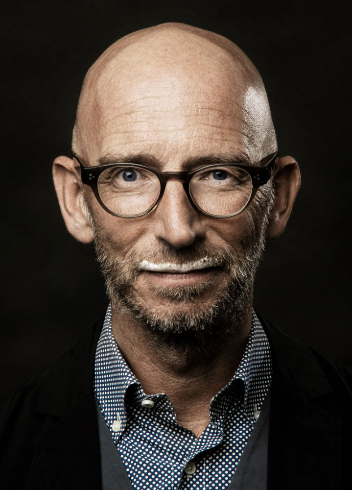 Eine glatzköpfige Person trägt Brille, Hemd, Sakko, hat ein weißes Lächeln. Fürstenberg Porzellan.