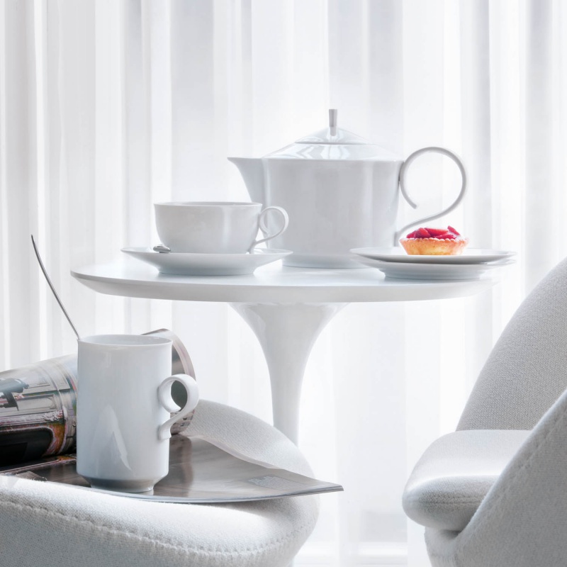Weißes Porzellan-Service auf rundem Tisch, Törtchen neben Tasse, helle Umgebung. Fürstenberg Porzellan.