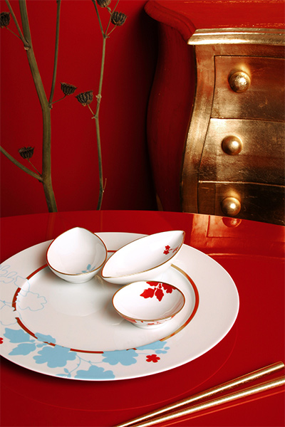 Weiße Porzellanschalen und Teller mit roten, blauen Blumenmotiven auf rotem Tisch. Fürstenberg Porzellan.
