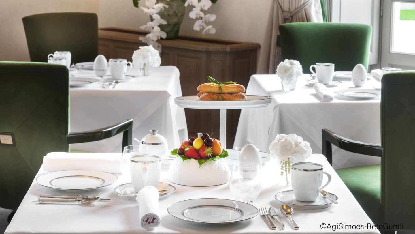 Weiß gedeckter Tisch mit Obstschale, Gebäck und Blumendekoration im eleganten Restaurant. Fürstenberg Porzellan.