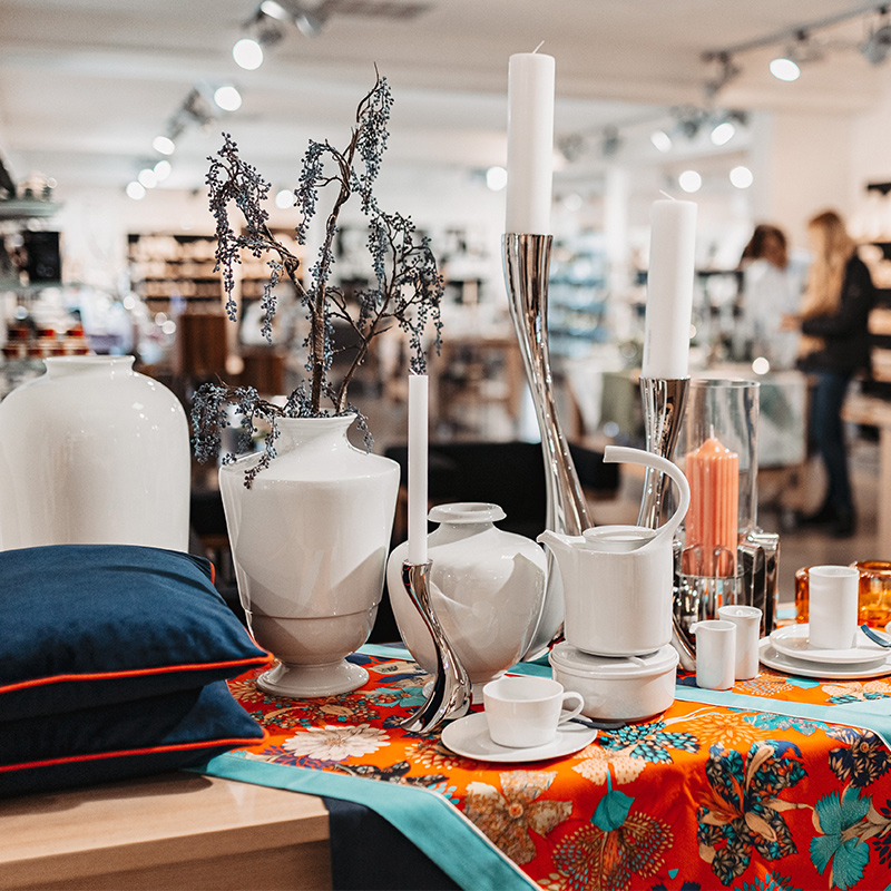 Porzellanvasen und Kerzen auf floral bedecktem Tisch in modernem Showroom. Fürstenberg Porzellan.
