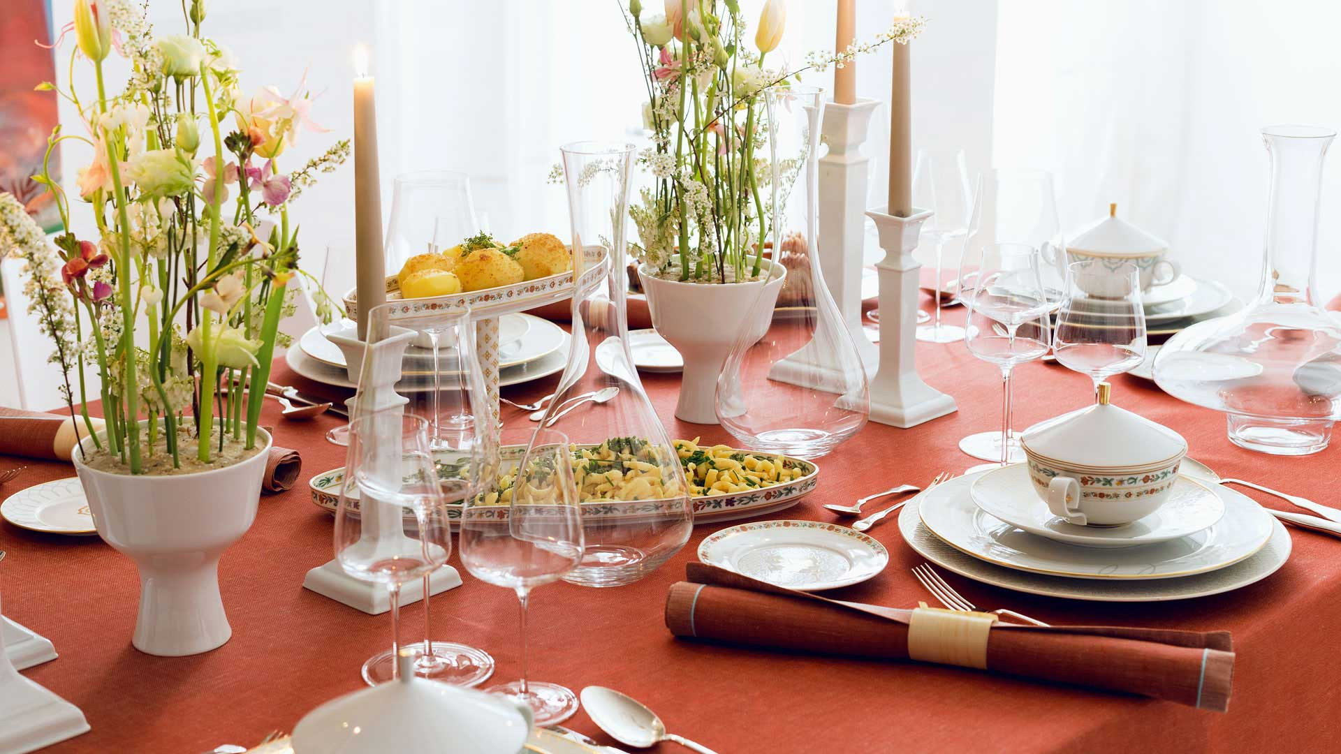 Elegante Tischdekoration mit weißem Porzellangeschirr und Blumen auf roter Tischdecke. Fürstenberg Porzellan.
