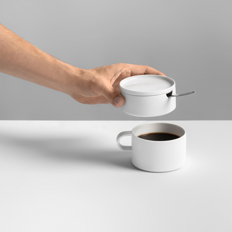 Eine Hand hält eine weiße Zuckerdose über einer Tasse Kaffee. Fürstenberg Porzellan.