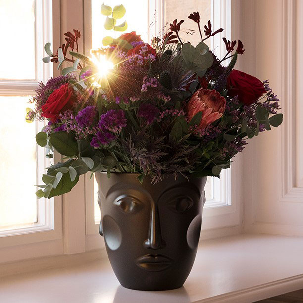 Schwarze Gesichtsvase hält bunte Blumen vor einem sonnigen Fenster. Fürstenberg Porzellan.