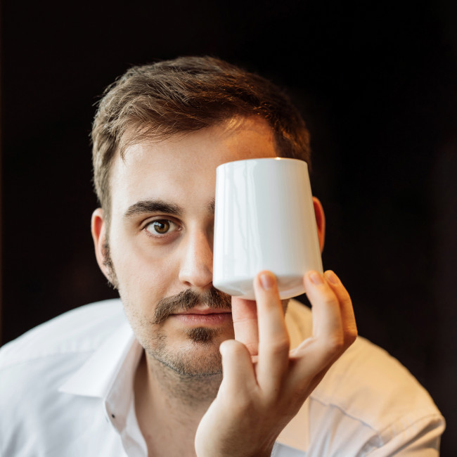 Eine Person hält eine weiße Tasse vor einem Auge. Fürstenberg Porzellan.