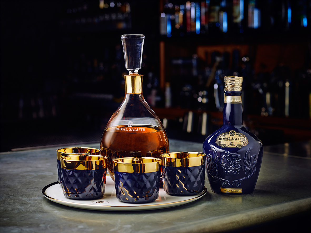 Dekanter und Flasche „Royal Salute“ neben goldgeränderten Tassen auf Tablett, Barhintergrund. Fürstenberg Porzellan.