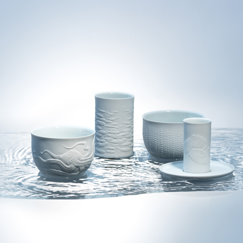 Porzellantassen und -becher mit maritimen Motiven stehen auf reflektierender Wasseroberfläche. Fürstenberg Porzellan.