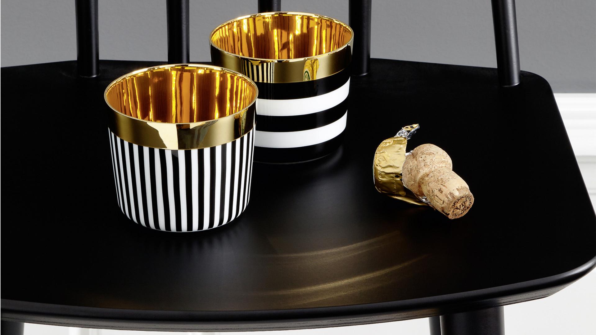 Zwei schwarz-weiß gestreifte Becher mit goldener Innenfläche, auf schwarzem Tisch. Fürstenberg Porzellan.