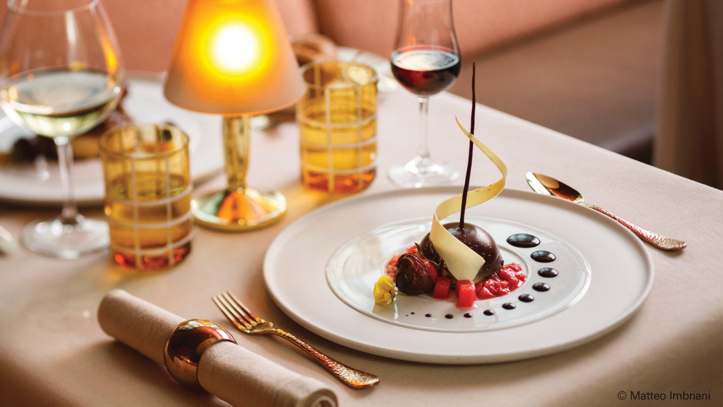 Dessert auf weißem Teller, dekoriert, auf elegant gedecktem Tisch mit Getränken. Fürstenberg Porzellan.
