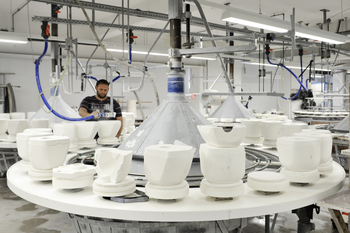 Porzellanherstellung, Arbeiter bedient Gießanlage, umgeben von Tonformen in Fabrik. Fürstenberg Porzellan.