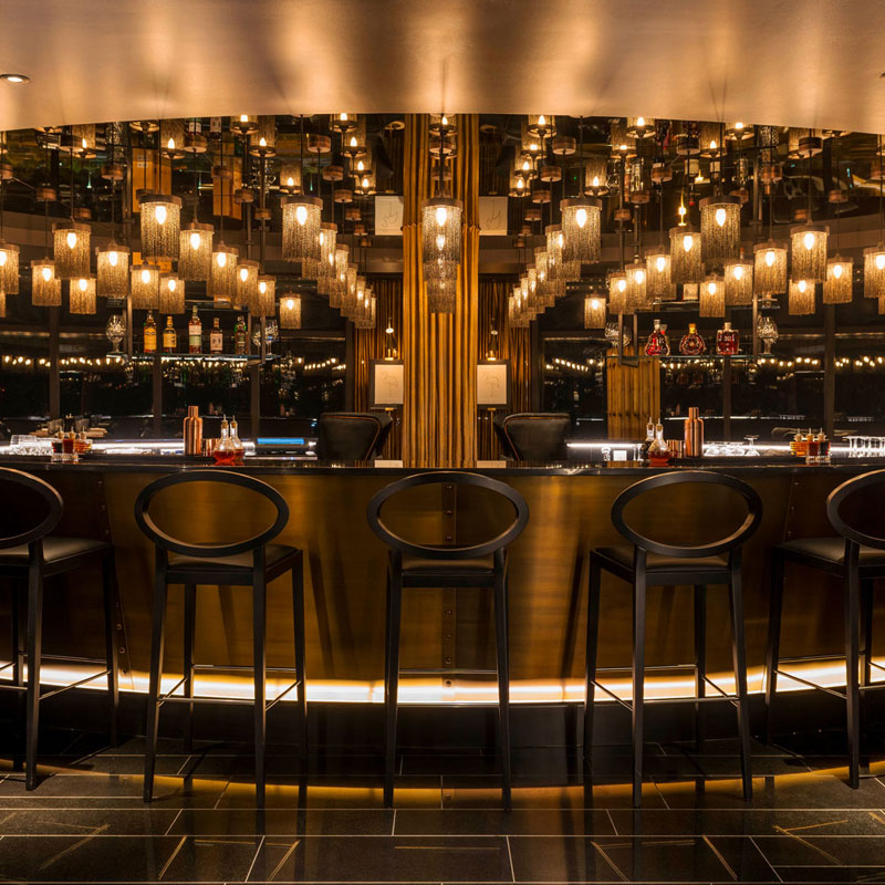 Elegante Bar mit schwarzen Stühlen, goldener Einrichtung, leuchtenden Lampen spiegelt gemütliche Atmosphäre wider. Fürstenberg Porzellan.