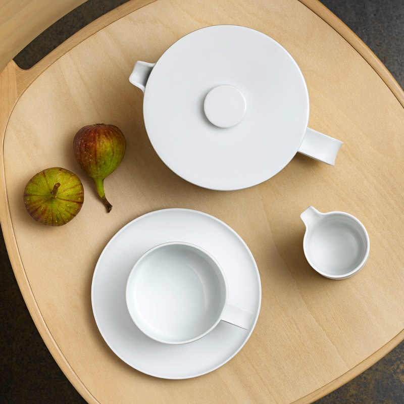 Weiße Teekanne, Tasse und Milchkännchen auf Holztisch neben zwei Feigen. Fürstenberg Porzellan.