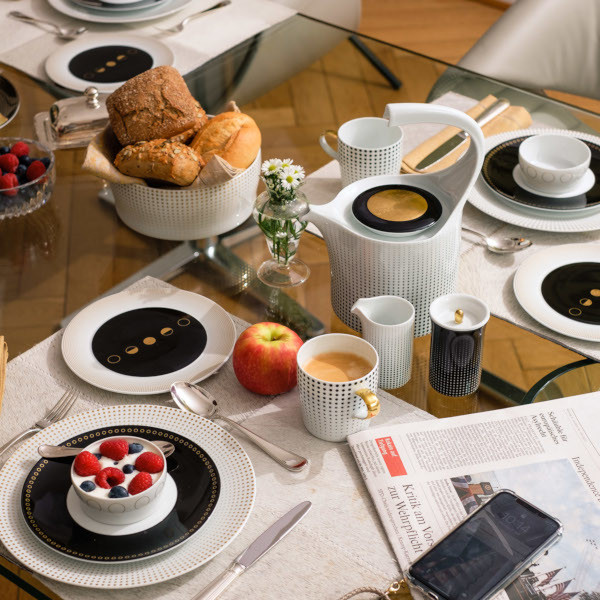 Frühstückstisch mit Geschirr, Kaffee, Brötchen und Früchten auf Glastisch. Fürstenberg Porzellan.