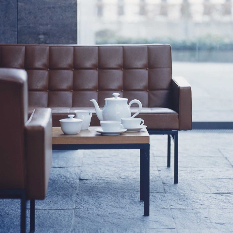 Teekanne und Tassen stehen auf Couchtisch zwischen braunen Sofas im modernen Raum. Fürstenberg Porzellan.