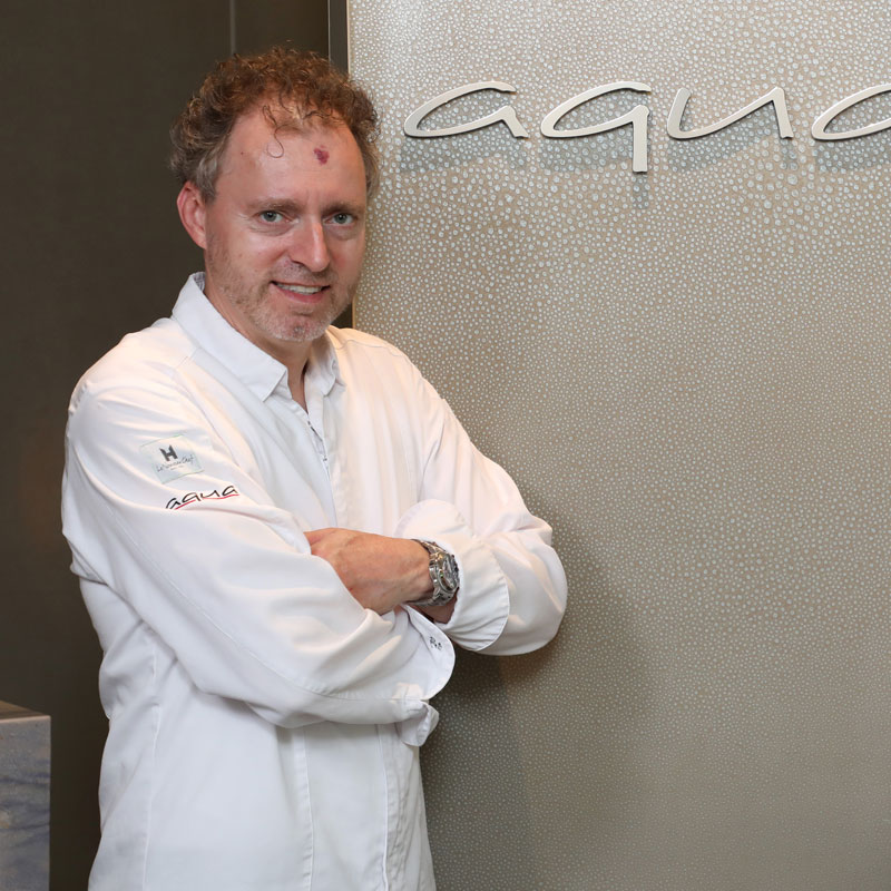 Mann in weißem Hemd steht vor einer Wand mit "aqua" Schriftzug. Fürstenberg Porzellan.
