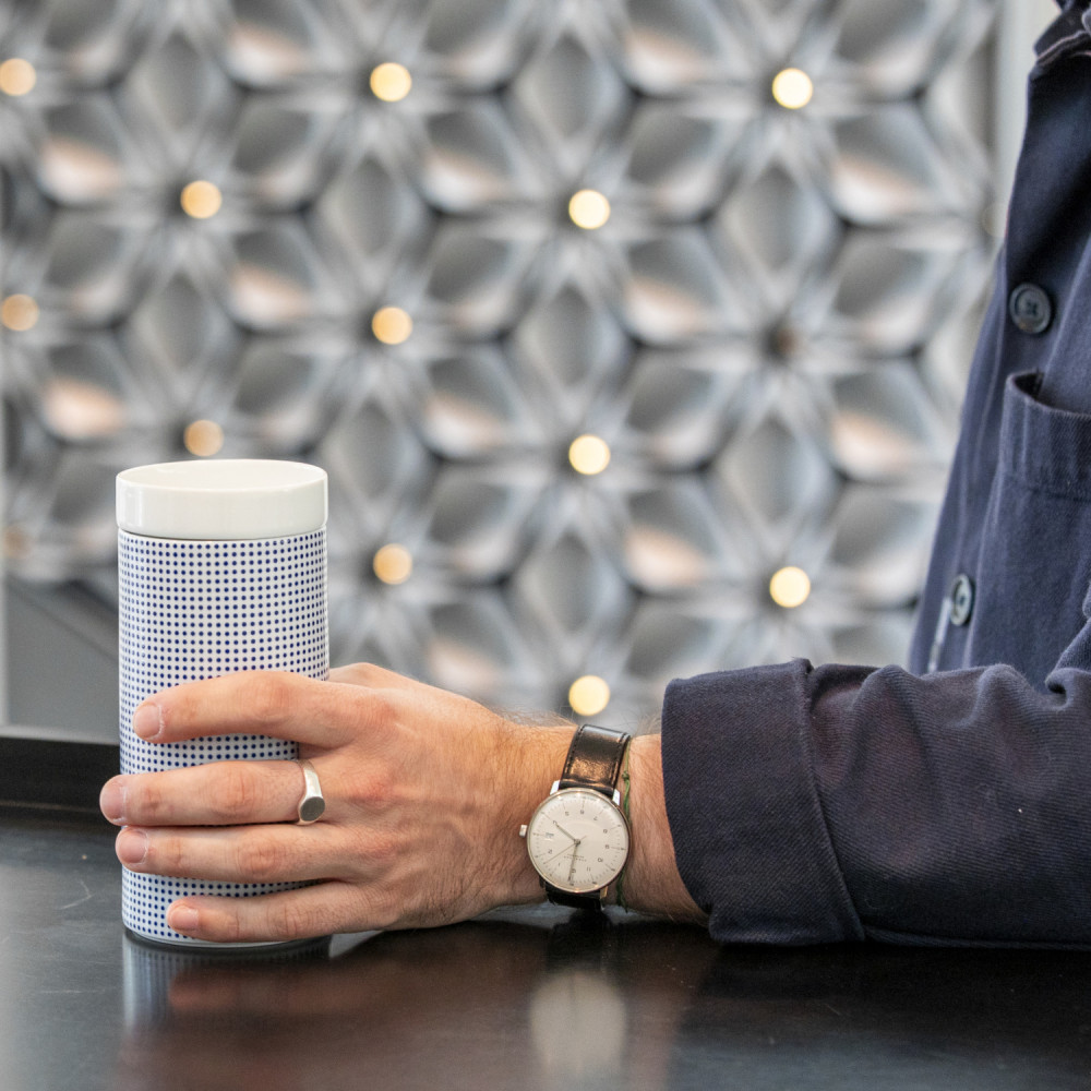 Hand hält elegante, gemusterte Vase auf schwarzer Theke vor kunstvoller Wand. Fürstenberg Porzellan.