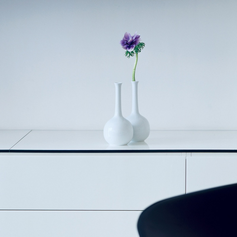 Zwei weiße Vasen mit lilafarbener Blume auf weißem Tisch, minimalistisch. Fürstenberg Porzellan.