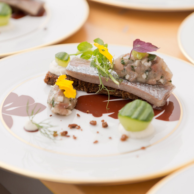 Fein angerichteter Fisch mit Kräutern und essbaren Blüten auf Porzellanteller. Fürstenberg Porzellan.