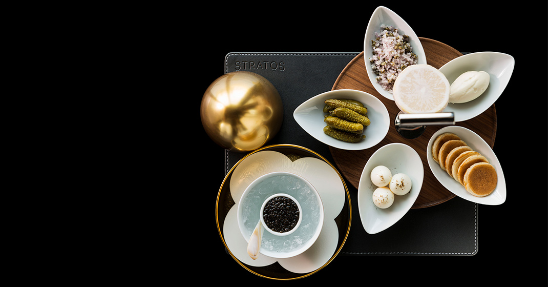 Kaviar-Set mit Beilagen auf weißem Porzellan, daneben goldene Kugel, "STRATOS". Fürstenberg Porzellan.