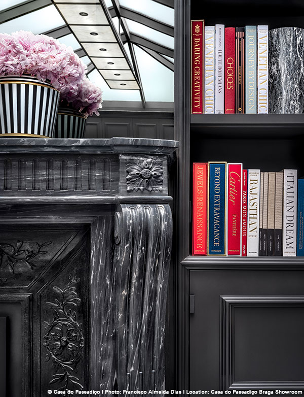 Schwarz-weißer Marmorkamin, Blumen in gestreifter Vase; Bücherregal mit bunten Büchern rechts. Fürstenberg Porzellan.