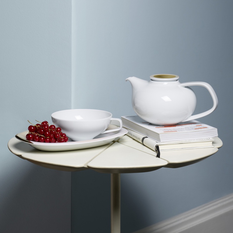 Teekanne steht auf Büchern, daneben Schale mit Johannisbeeren auf kleinem Tisch. Fürstenberg Porzellan.