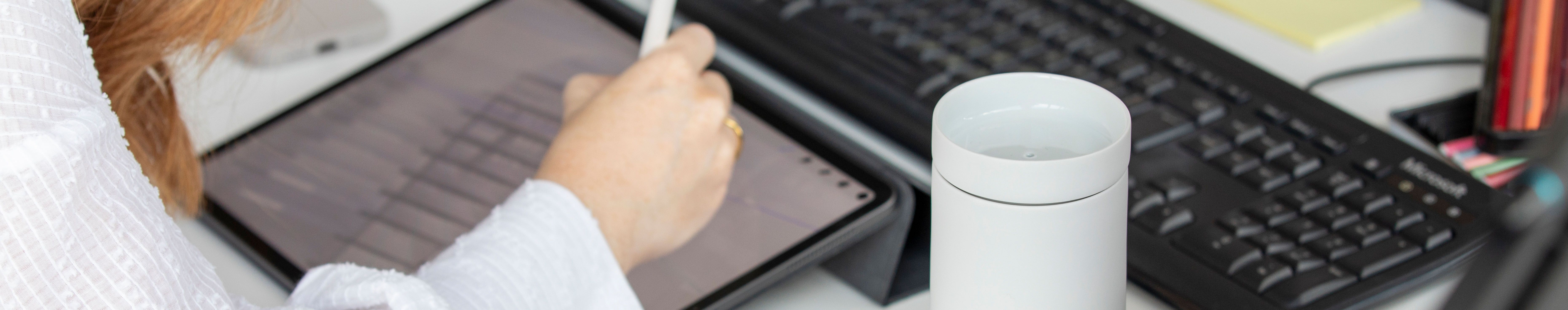 Person benutzt Tablet mit Stift, daneben Tastatur und weißer Becher. Fürstenberg Porzellan.