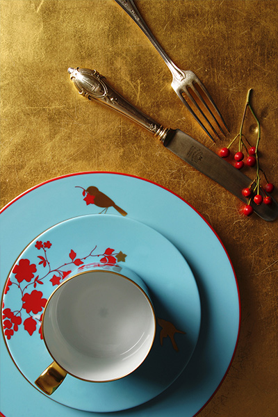 Blauer Teller mit rotem Blumenmuster, darauf Tasse; Gabel, Messer, Beeren daneben. Fürstenberg Porzellan.