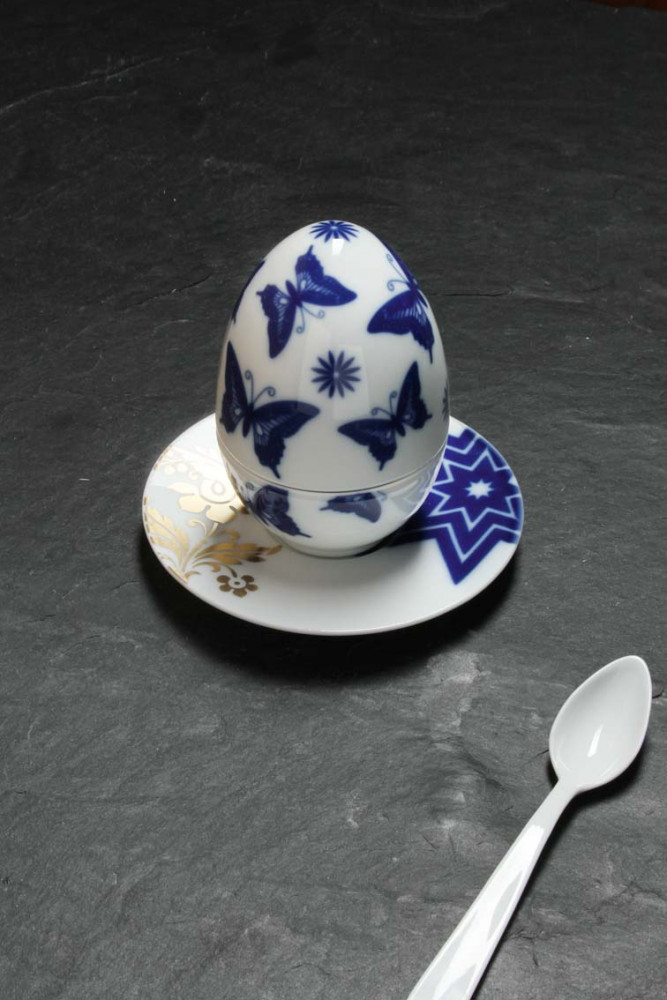 Porzellanei mit blauen Schmetterlingen steht auf Untertasse neben Löffel. Fürstenberg Porzellan.
