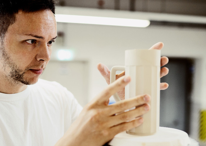 Mann inspiziert sorgfältig eine elfenbeinfarbene Tasse in einer Werkstatt. Fürstenberg Porzellan.