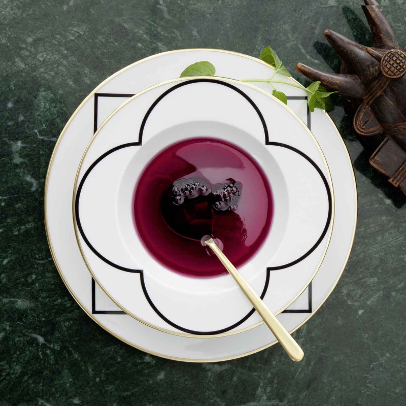 Schwarze Suppe in weißem Teller mit goldener Löffel auf grünem Tisch. Fürstenberg Porzellan.