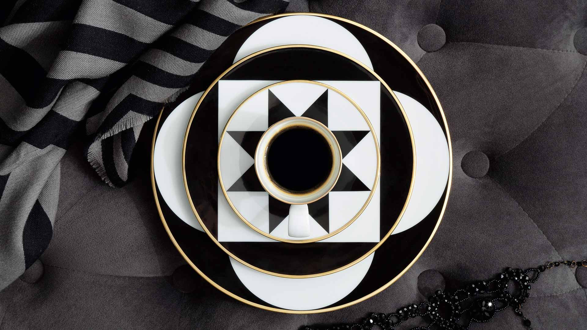 Kaffeetasse steht auf schwarz-weißem geometrischem Muster, umgeben von Tellern, Stoff und Perlen. Fürstenberg Porzellan.