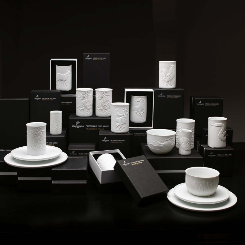Weiße Porzellanbecher und Schalen mit Reliefs stehen auf schwarzen Verpackungen. Fürstenberg Porzellan.