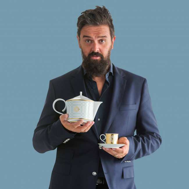 Mann hält Porzellan-Teekanne und Tasse vor blauem Hintergrund. Fürstenberg Porzellan.