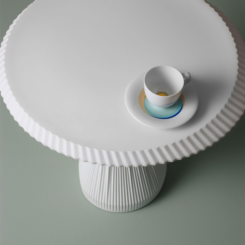 Weiße Tasse auf geriffeltem Tisch mit bunter Untertasse. Fürstenberg Porzellan.
