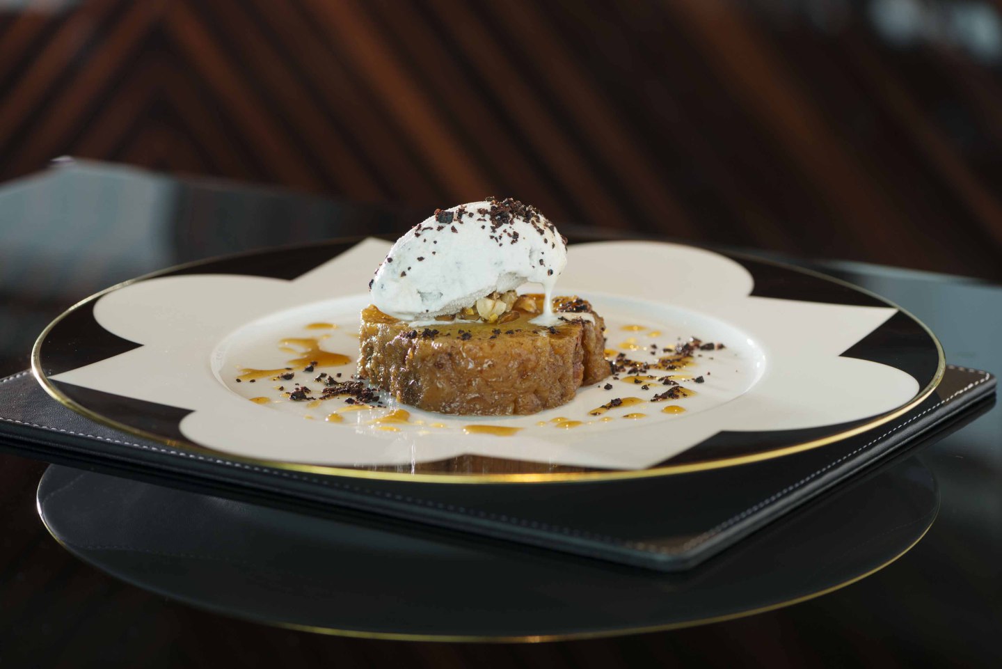 Dessert auf Teller, dekoriert mit Eiscreme und Soße, auf schwarzem Untergrund. Fürstenberg Porzellan.