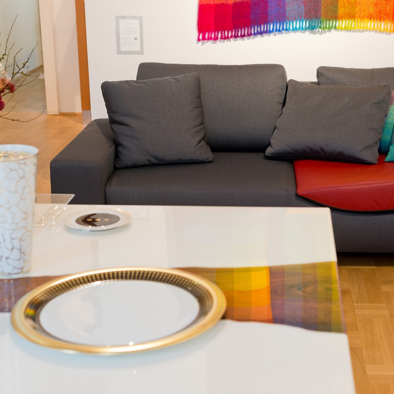 Teller auf weißem Tisch vor grauem Sofa mit buntem Tuch. Fürstenberg Porzellan.