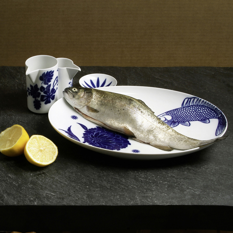 Fisch liegt auf blau-weißem Teller, daneben halbierte Zitronen, Kannen. Fürstenberg Porzellan.
