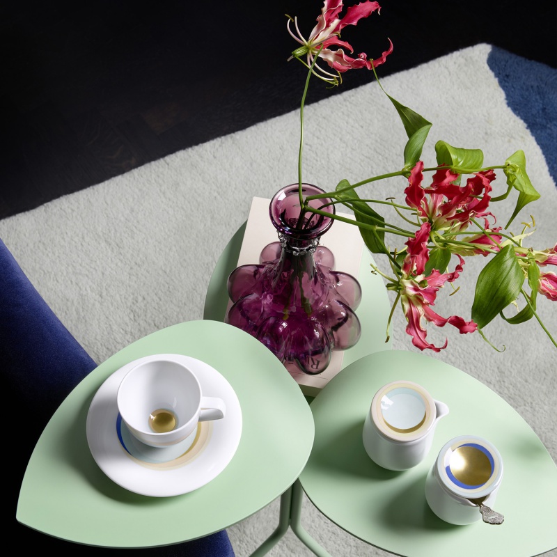 Porzellantassen und Vase stehen auf grünem Tisch neben blauem Sofa. Fürstenberg Porzellan.