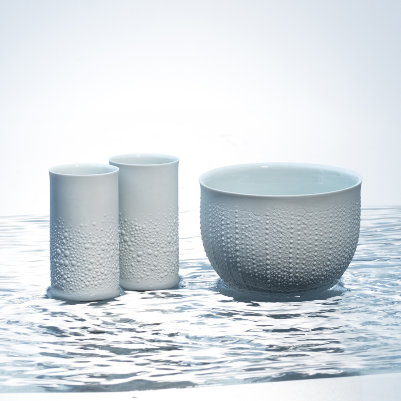 Zwei weiße Becher und Schale mit Struktur stehen auf Wasseroberfläche. Fürstenberg Porzellan.