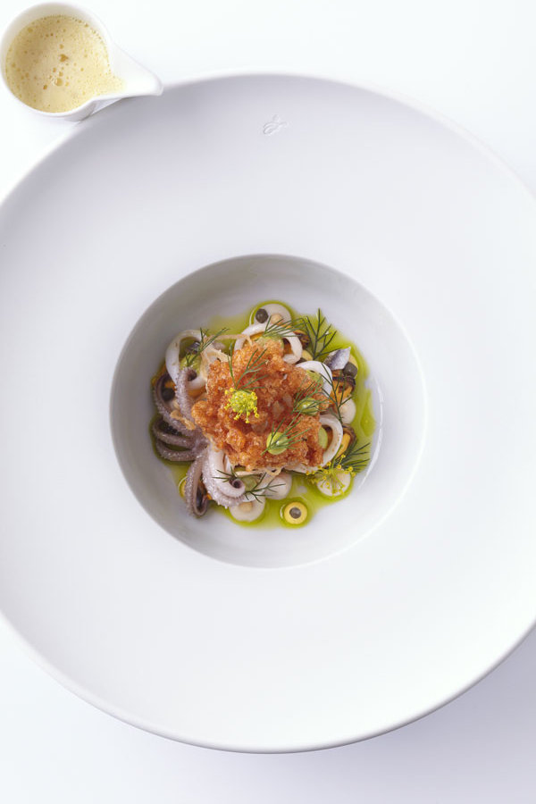 Gourmetgericht auf weißem Porzellanteller, dekoriert mit Kräutern, daneben kleine Sauciere. Fürstenberg Porzellan.
