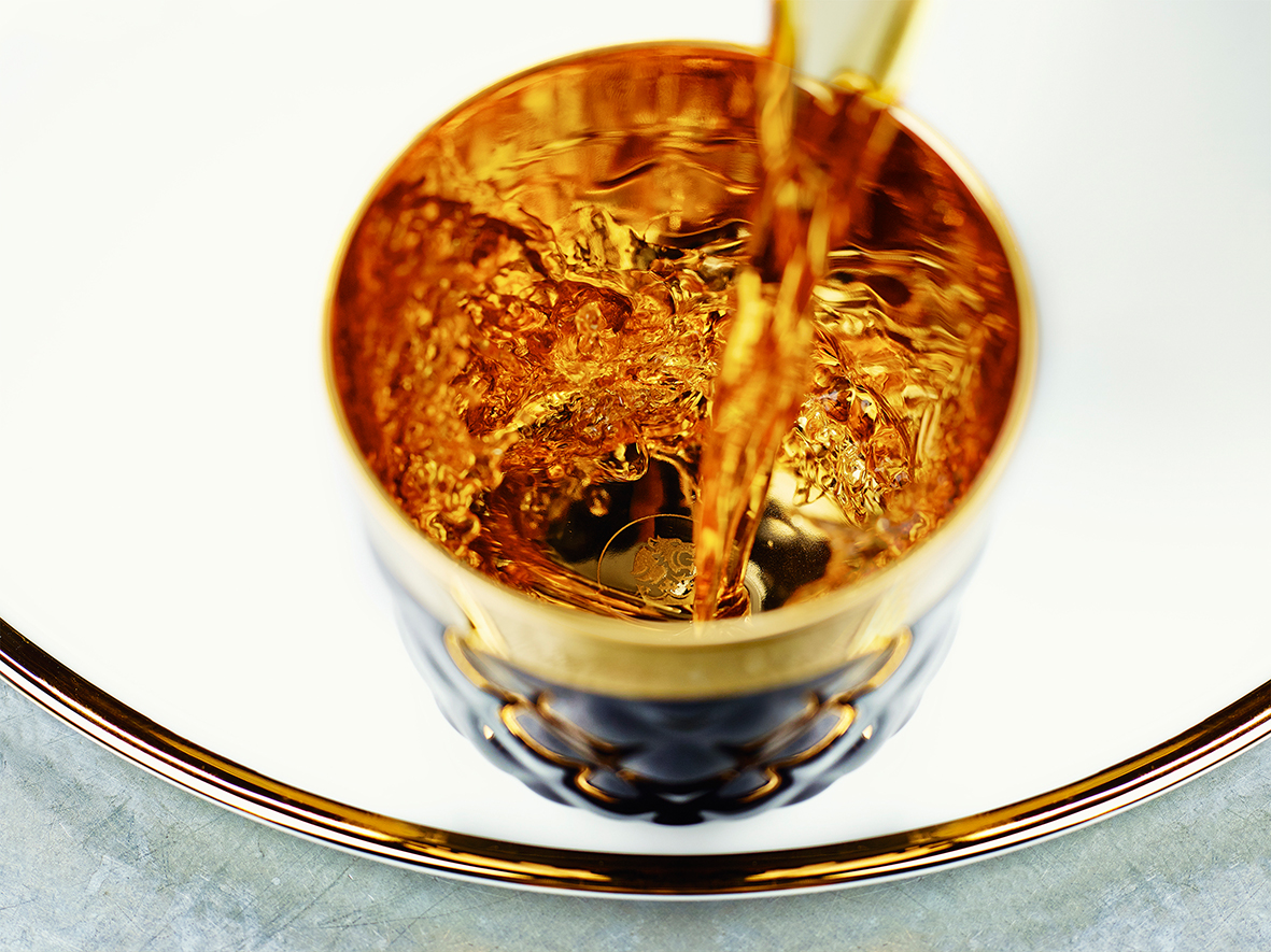 Goldene Flüssigkeit wird in einen verzierenden, glänzenden Becher gegossen. Fürstenberg Porzellan.