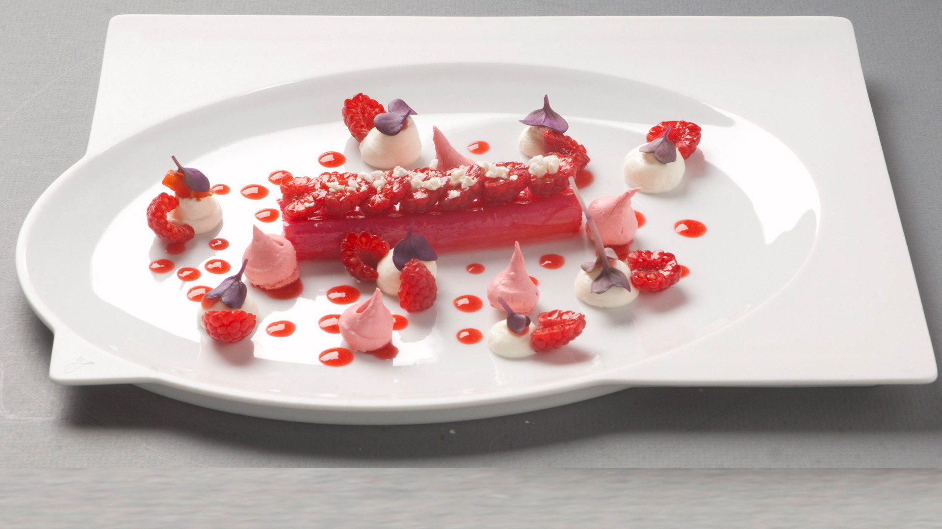 Himbeer-Dessert mit Sahnetupfen und Soße auf weißem ovalen Teller arrangiert. Fürstenberg Porzellan.