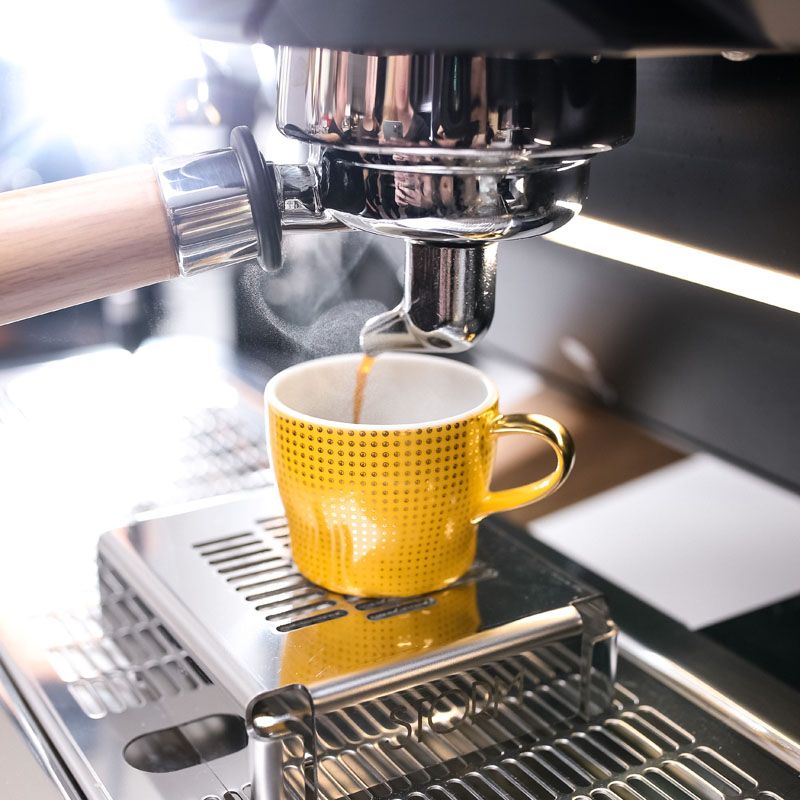 Espressomaschine brüht Kaffee in gelbe Tasse mit Punktmuster. Fürstenberg Porzellan.