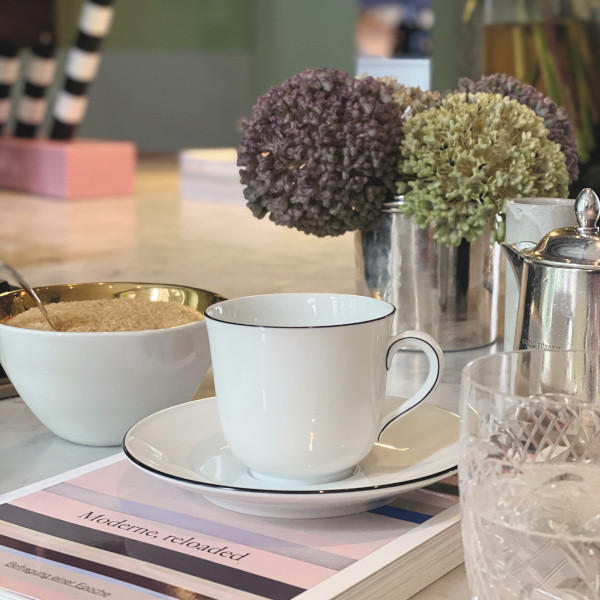 Weiße Porzellantasse auf Untertasse neben Zuckerschale, Buch und Blumenstrauß. Fürstenberg Porzellan.