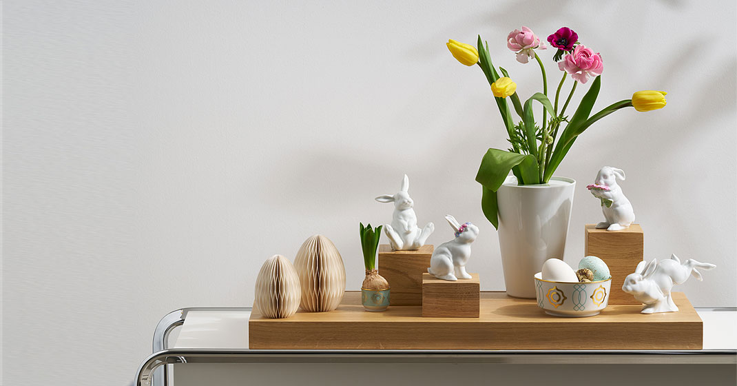 Porzellan-Hasenfiguren und bunte Blumen auf Holzbrettern dekoriert. Fürstenberg Porzellan.