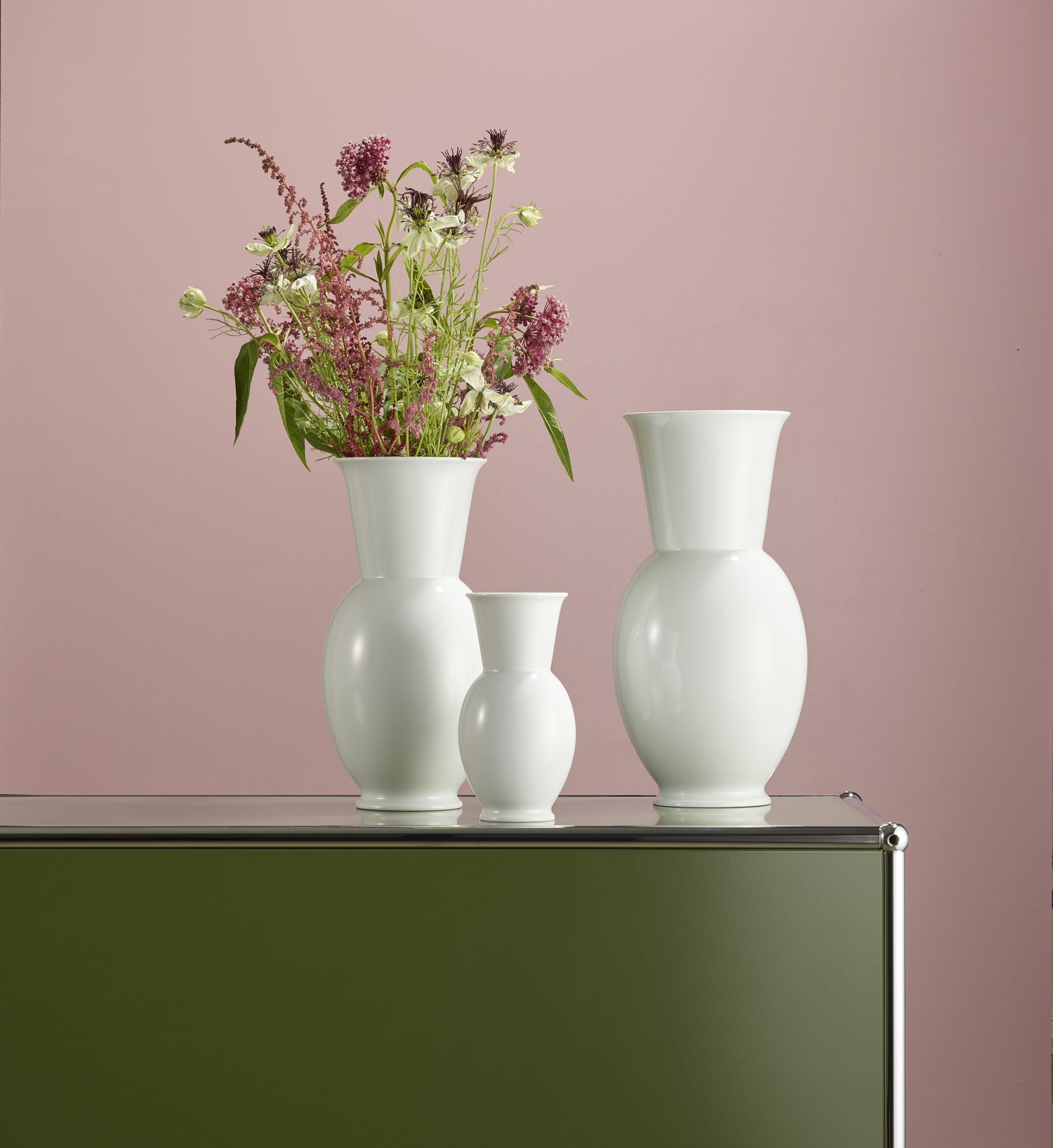 Weiße Porzellan-Vasen mit Blumen auf grünem Schrank, rosa Wandhintergrund. Fürstenberg Porzellan.