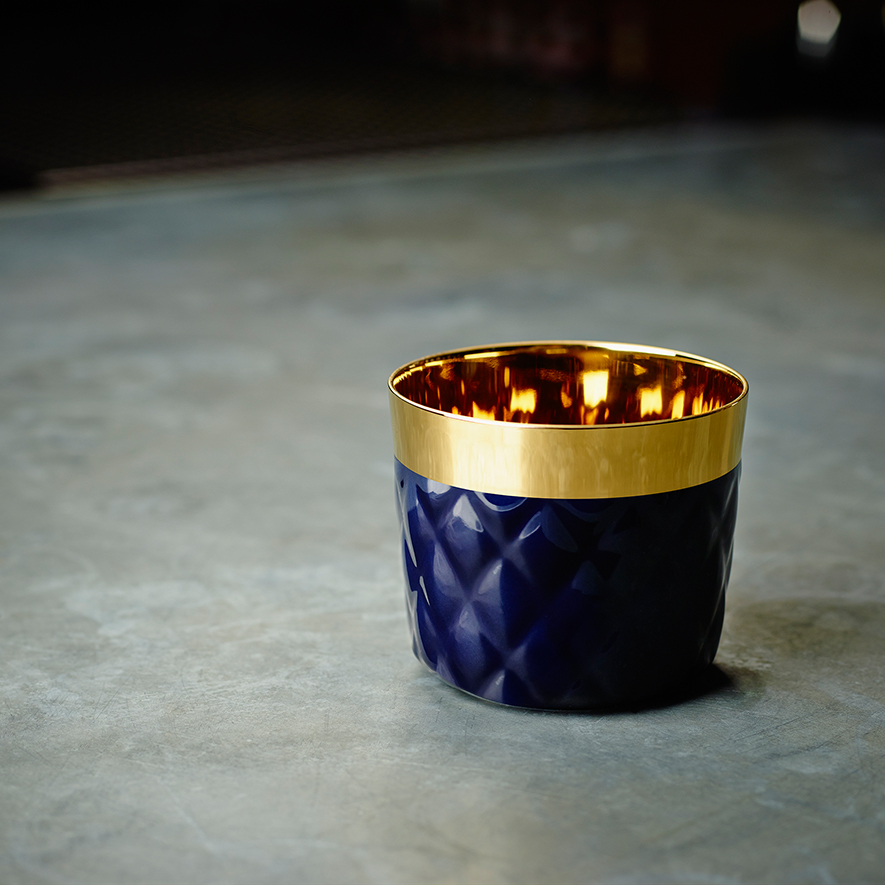 Dunkelblaue Teelichthalter mit goldener Innenfläche steht auf grauem Untergrund. Fürstenberg Porzellan.